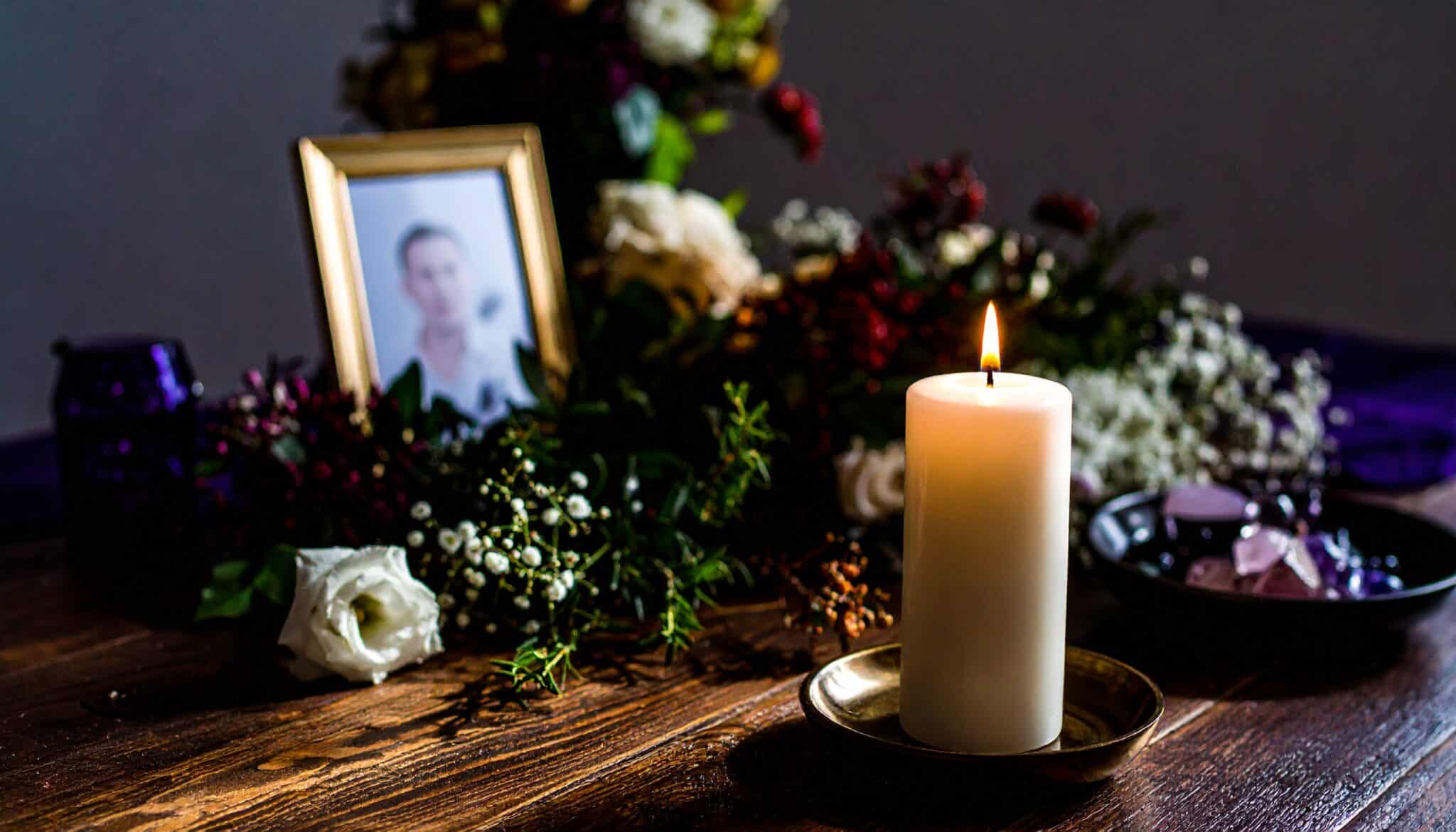 Death Anniversary Alter: A softly lit candle on a full wooden table surrounded by forget-me-nots, chrysanthem