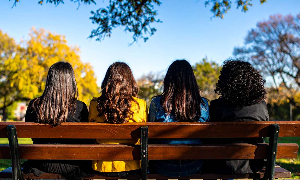 Four women sitting together on a bench in quiet connection, symbolizing the return of belonging and emotional support after grief.