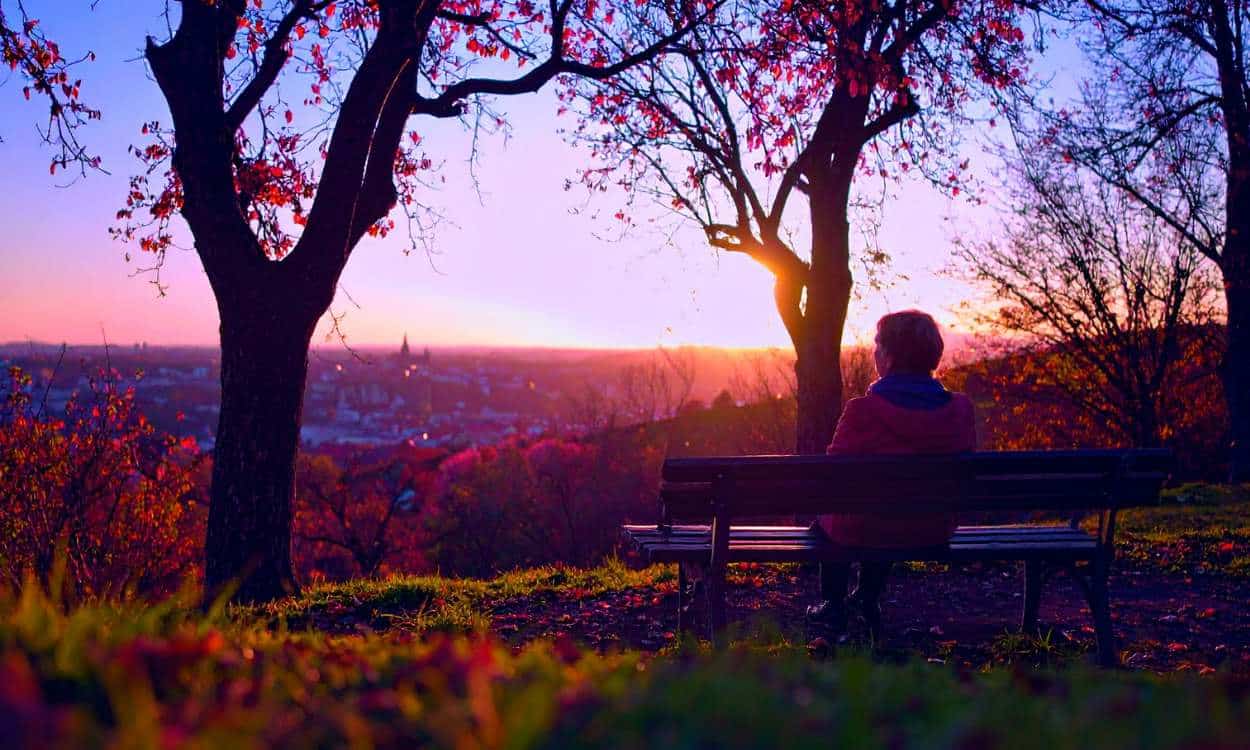 Middle-aged woman sitting alone on a park bench at sunset, reflecting quietly after the loss of a loved one, symbolizing emotional loneliness and grief.